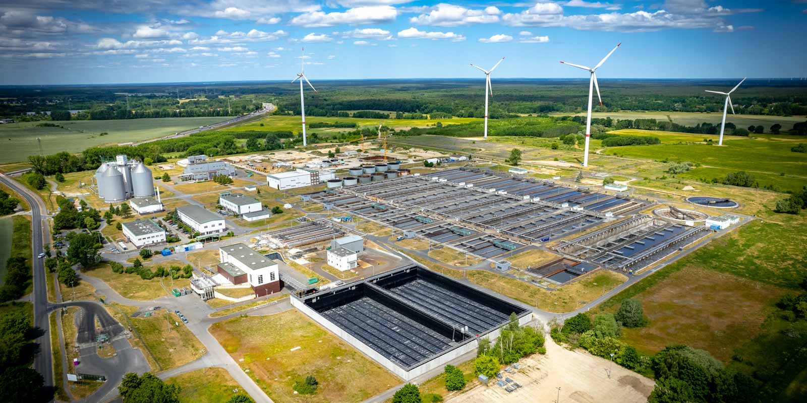 Komplette Abbildung des Klärwerks Schönerlinde aus der Luft mit Windrädern am Horiziont
