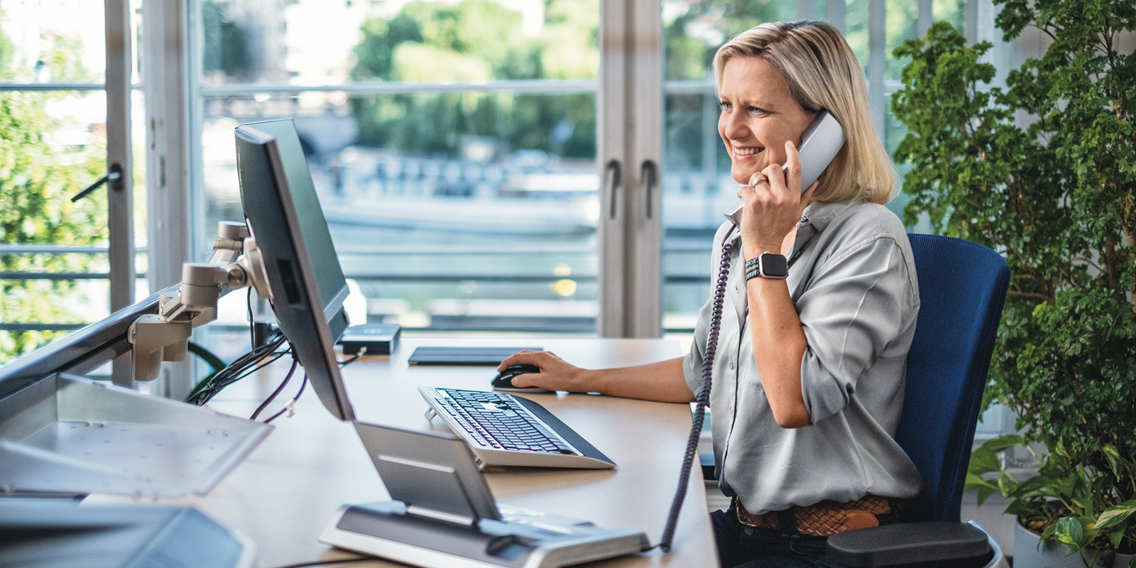Frau am Telefon in einem hellen Büro vor großen Fenstern
