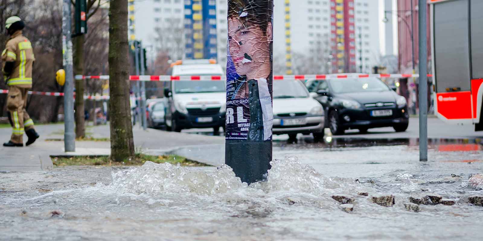 Rohrbruch auf einer Straße, an der an einer Laterne Wasser herausfließt