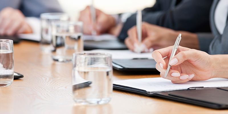 Leute sitzen an einem Besprechungstisch, Stifte in der HAnd und schreiben