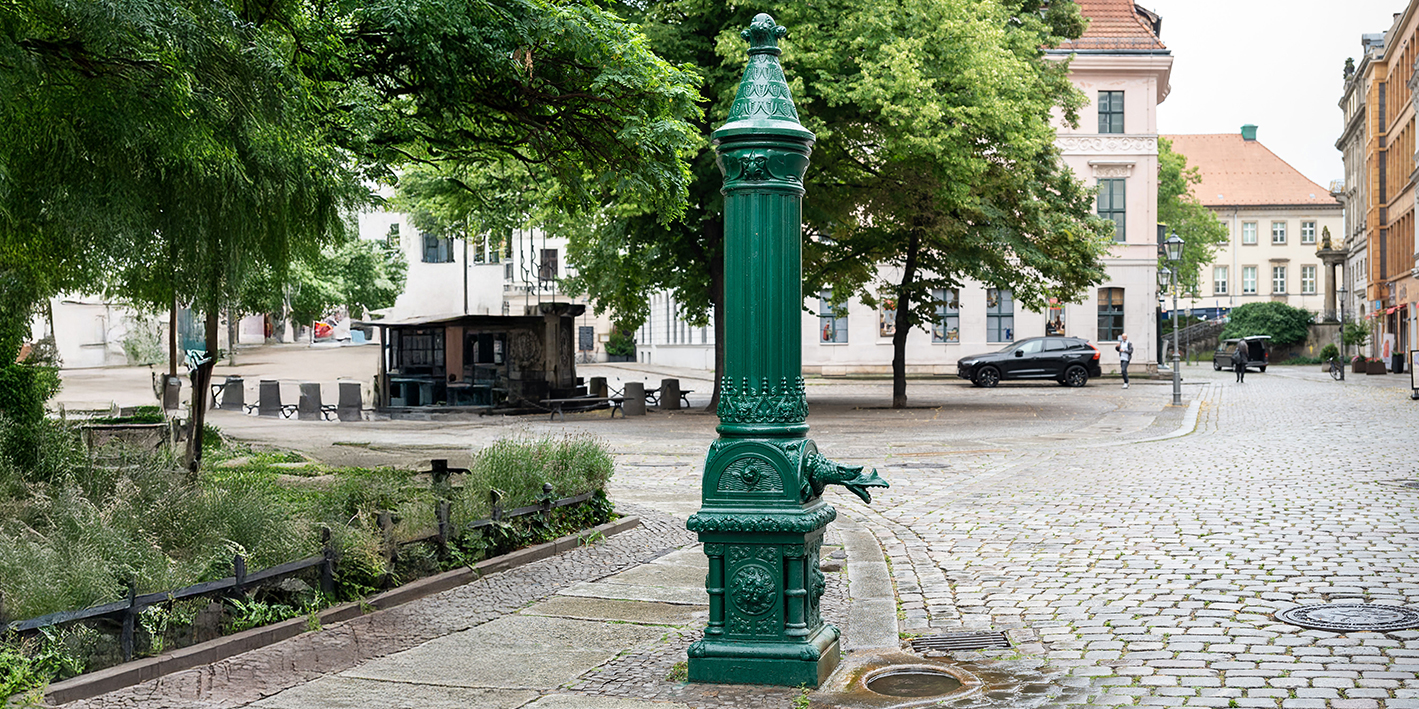 Eine alte grüne Schwengelpumpe am Straßenrand, die als Notwasserbrunnen fungiert
