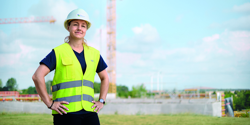 Frau mit Bauhelm und Warnweste steht auf einer Baustelle