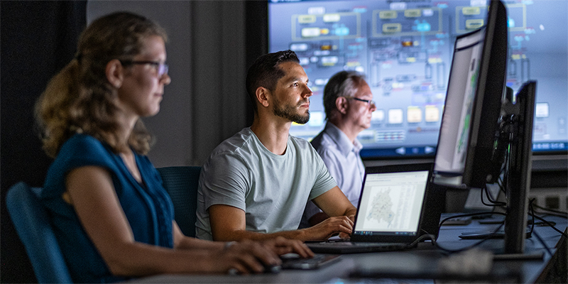 Drei IT-Kräfte arbeiten vor einem großen Touchscreen