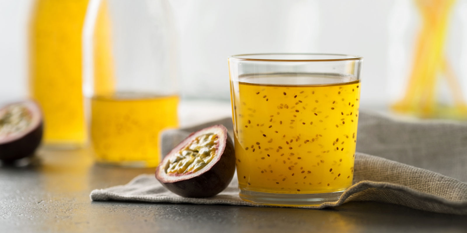 Ein Glas steht in der Küche. Es ist gefüllt mit Maracuja-Wasser und Chiasamen. Zur Dekoration liegen frische aufgeschnittene Maracujas aus. 