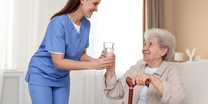 Schwester reicht alter Dame ein Glas Wasser