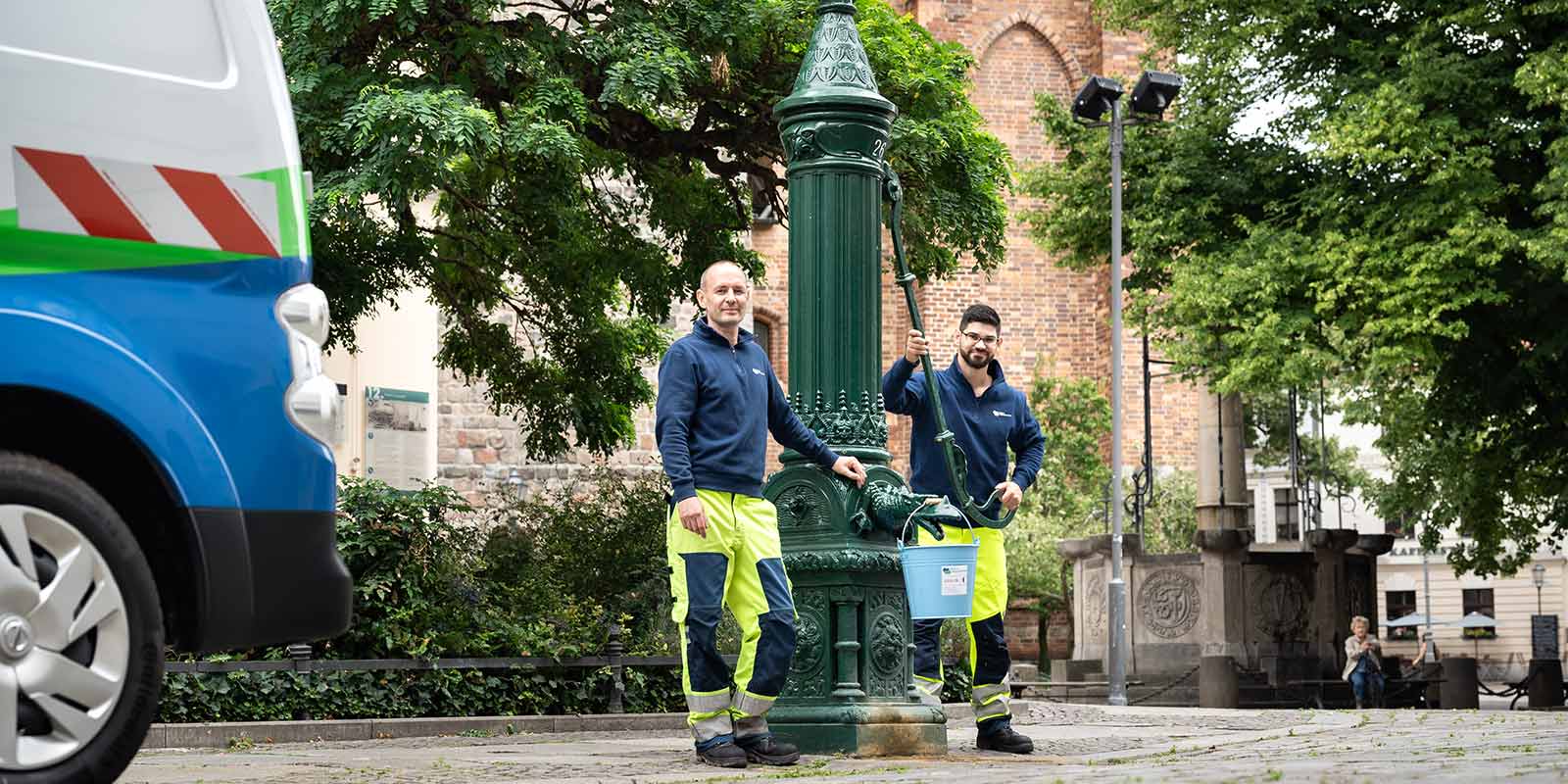 Zwei Mitarbeitende der Berliner Wasserbetriebe stehen an einer Schnwengelpumpe